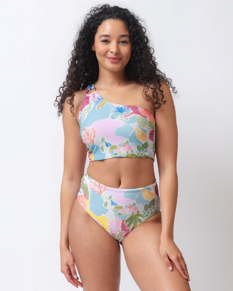 Photo of a woman wearing a colorful seashell inspired one-shoulder swim crop top and a colorful seashell inspired high waist swim bottom