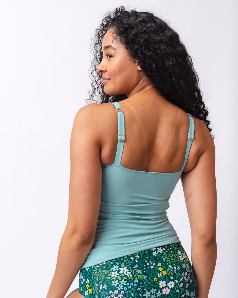 Photo of a woman wearing a light blue square neck swim tankini top and a green floral swim bottom- back angle