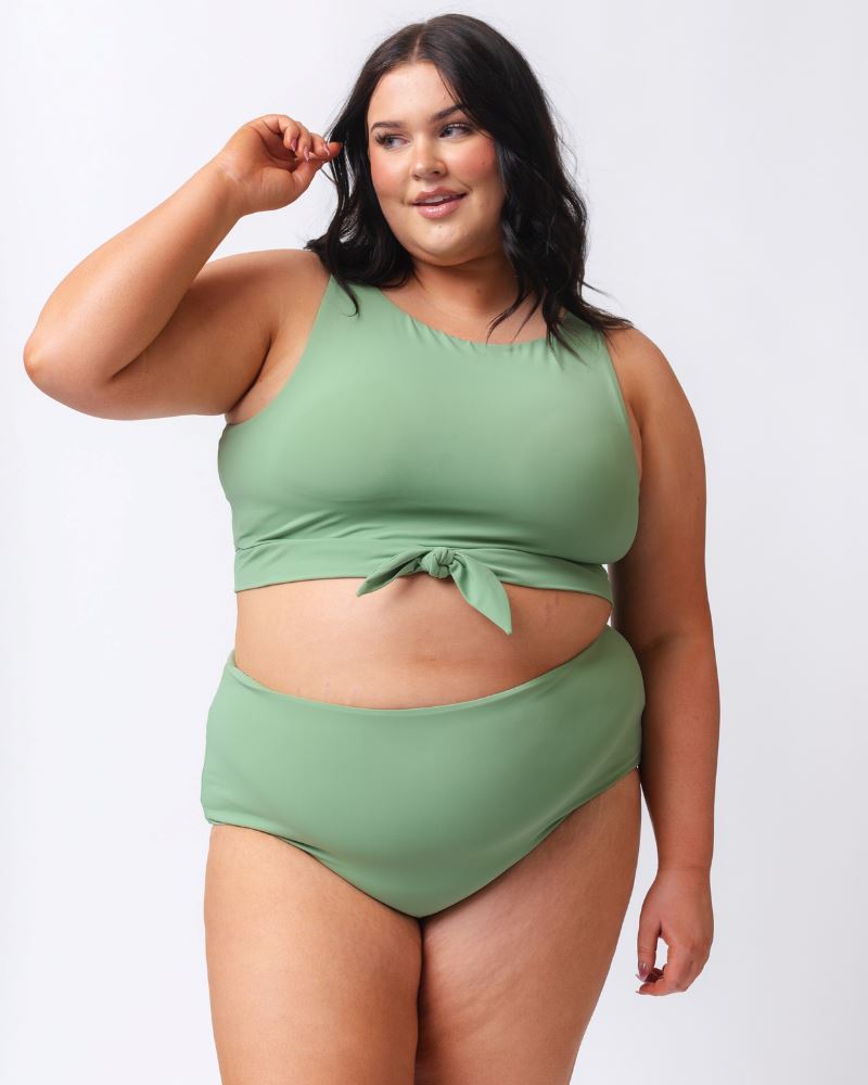 Photo of a woman wearing a light green knotted swim crop top and a dark green floral/ light green reversible swim bottom- light green side