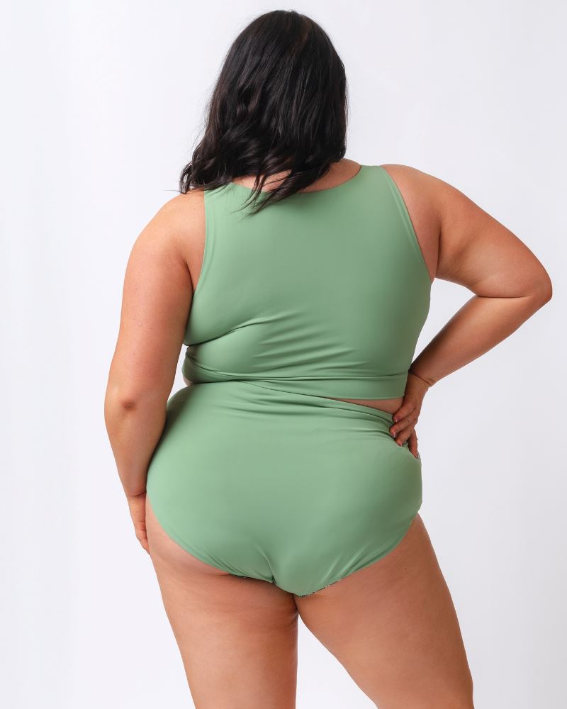 Photo of a woman wearing a light green knotted swim crop top and a dark green floral/ light green reversible swim bottom- light green side- back angle