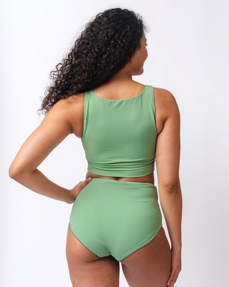 Photo of a woman wearing a light green knotted swim crop top and a dark green floral/ light green reversible swim bottom- light green side- back angle