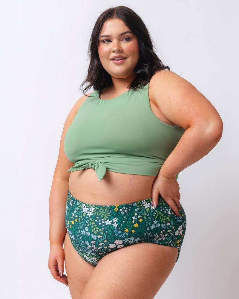 Photo of a woman wearing a light green knotted swim crop top and a dark green floral/ light green reversible swim bottom- floral side