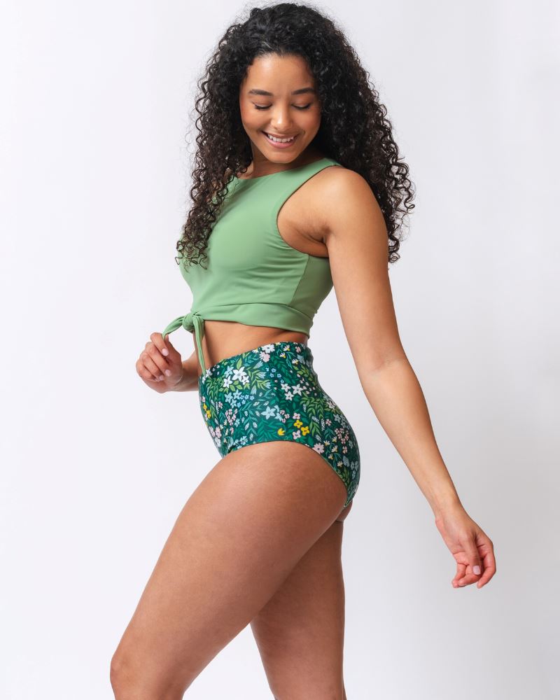 Photo of a woman wearing a light green knotted swim crop top and a dark green floral/ light green reversible swim bottom- floral side- side angle