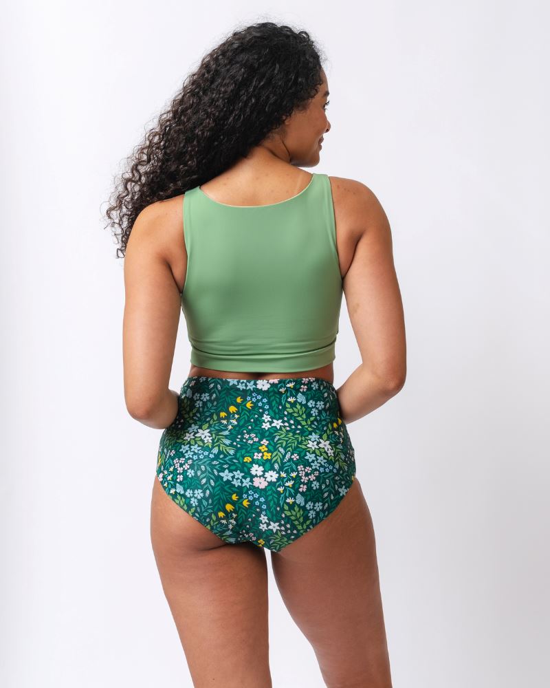 Photo of a woman wearing a light green knotted swim crop top and a dark green floral/ light green reversible swim bottom- floral side- back angle