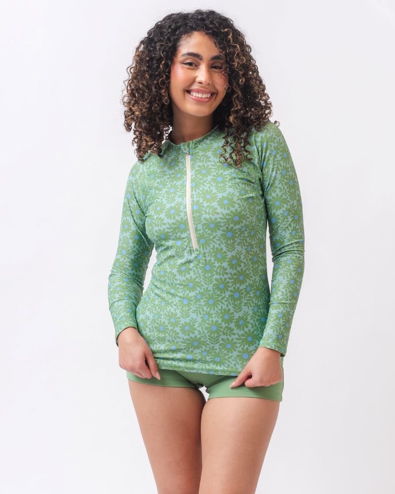Photo of a woman wearing a green floral long sleeve swim top with light green swim shorts