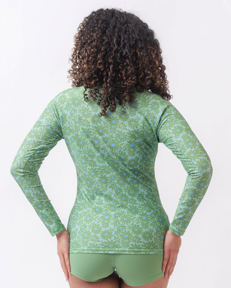 Photo of a woman with her back facing us wearing a green floral long sleeve swim top with light green swim shorts