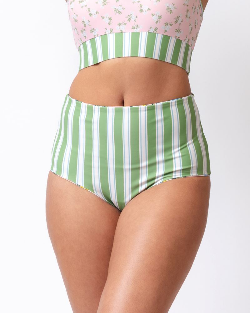 Close up photo of a woman wearing a green and white stripe high waist reversible swim bototms