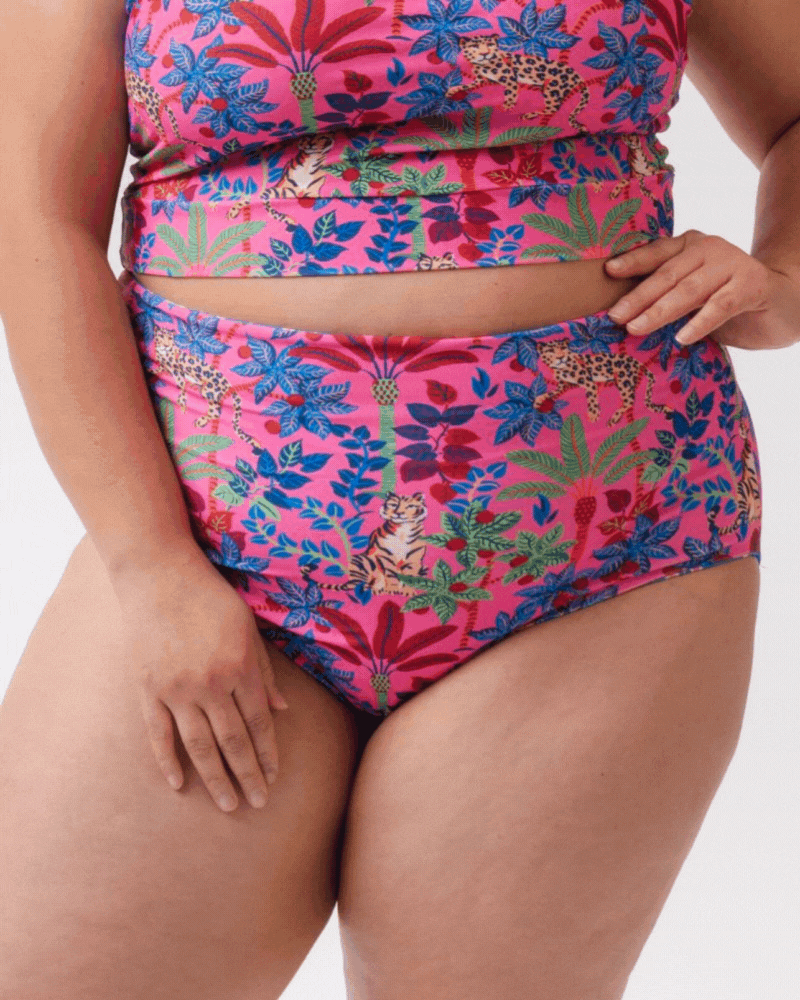Close up GIF of a woman wearing a bold pink print featuring tigers/ blue and pink floral reversible ultra high waist swim bottoms