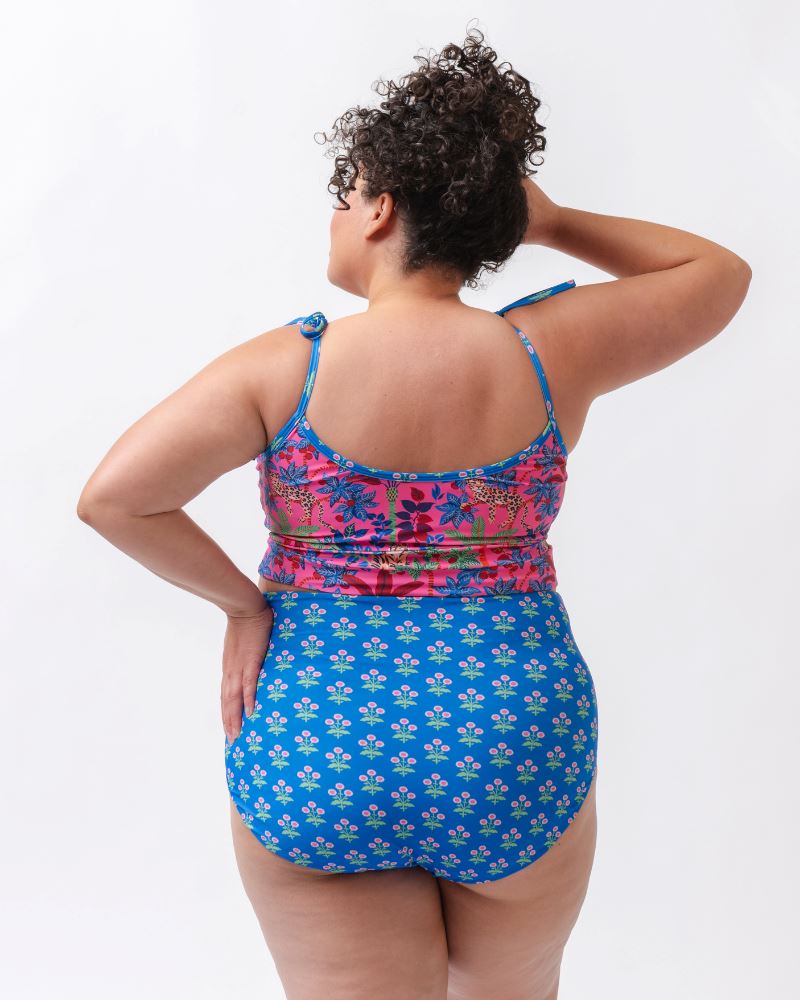 Photo of a woman wearing a bold pink print featuring tigers/ blue and pink floral reversible ultra high waist swim bottoms- floral side and a bold pink print featuring tigers shoulder-tie swim crop top- back angle