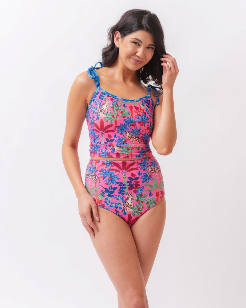 Photo of a woman wearing a bold pink print featuring tigers/ blue and pink floral reversible ultra high waist swim bottoms- tiger side and a matching shoulder-tie swim crop