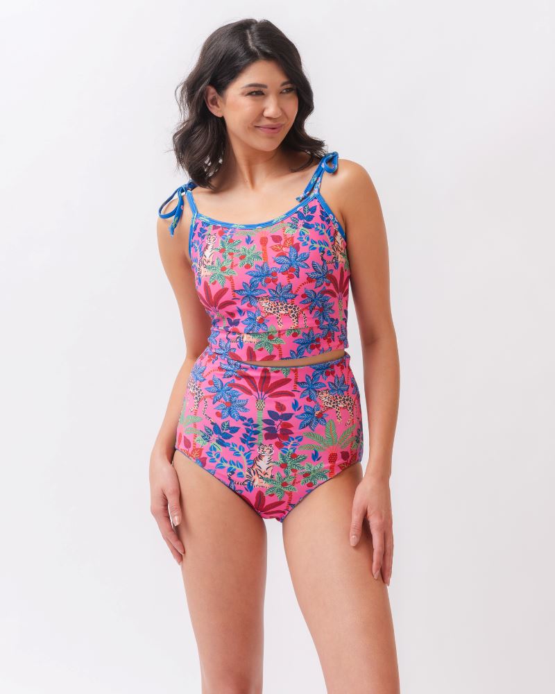 Photo of a woman wearing a bold pink and blue print featuring tigers and leopards shoulder-tie swim crop top and a bold pink print featuring tigers and leopards/ blue floral reversible swim bottom- tiger side