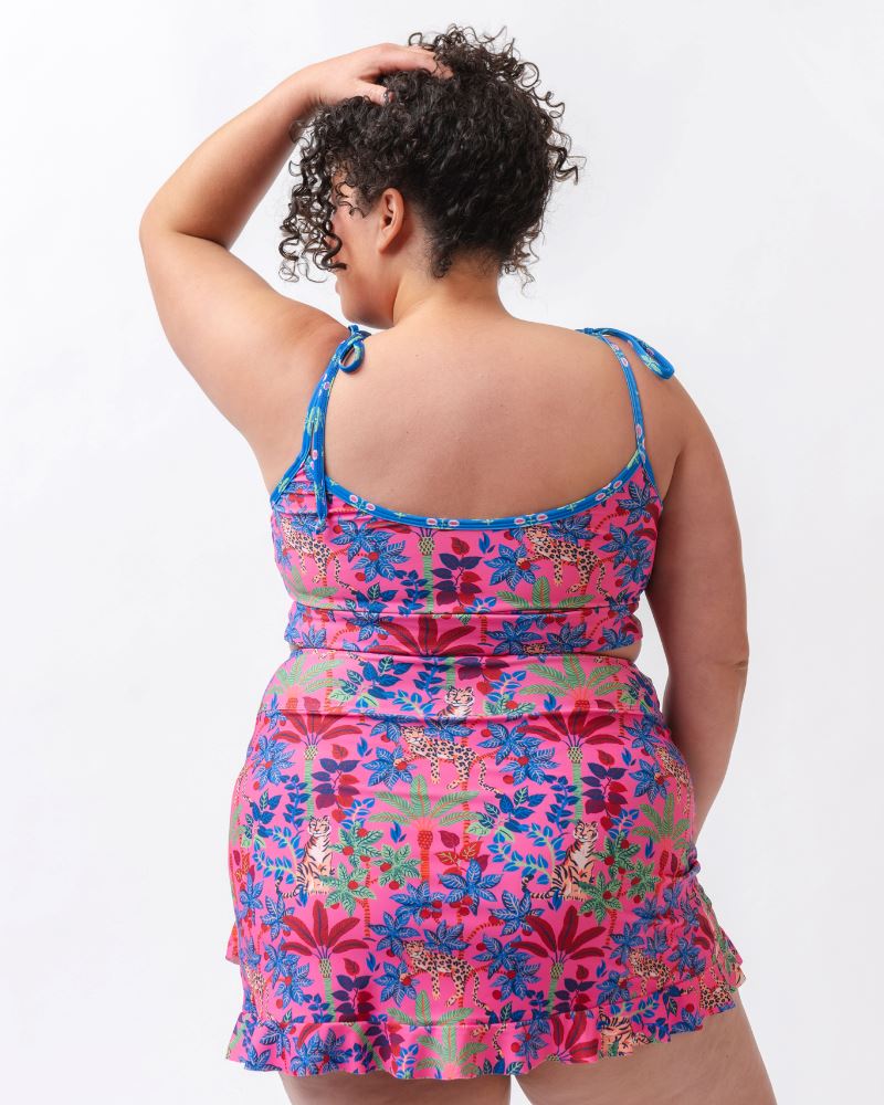 Photo of a woman wearing a bold pink and blue print featuring tigers and leopards swim skirt and a bold pink and blue print featuring tigers and leopards shoulder-tie swim crop top- back angle