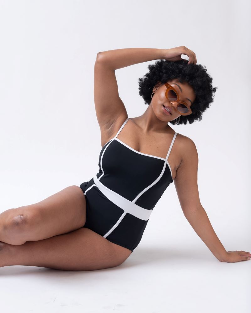 Photo of woman laying on her hip wearing a black and white classic one piece swims suit