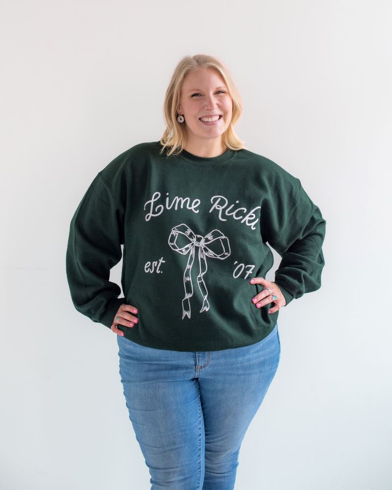 Photo of woman with her hands on her hips while wearing a green Lime Ricki crew neck sweatshirt with blue jeans