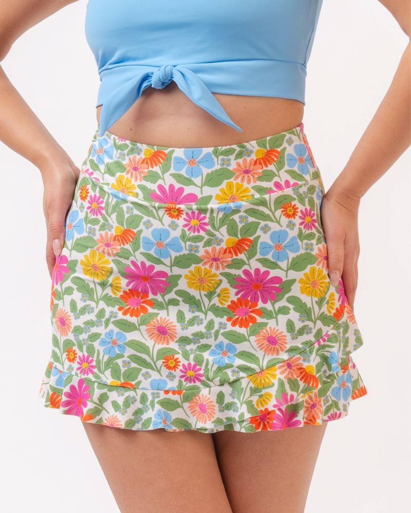 Close up photo of a woman wearing a light blue cropped swim top with a multi colored floral swim skirt
