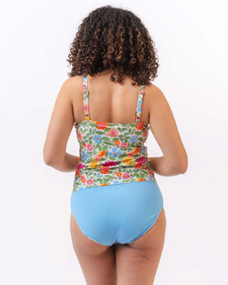 Photo of a woman with her back facing us wearing a multi colored floral swim tankini top with light blue high waist swim bottoms