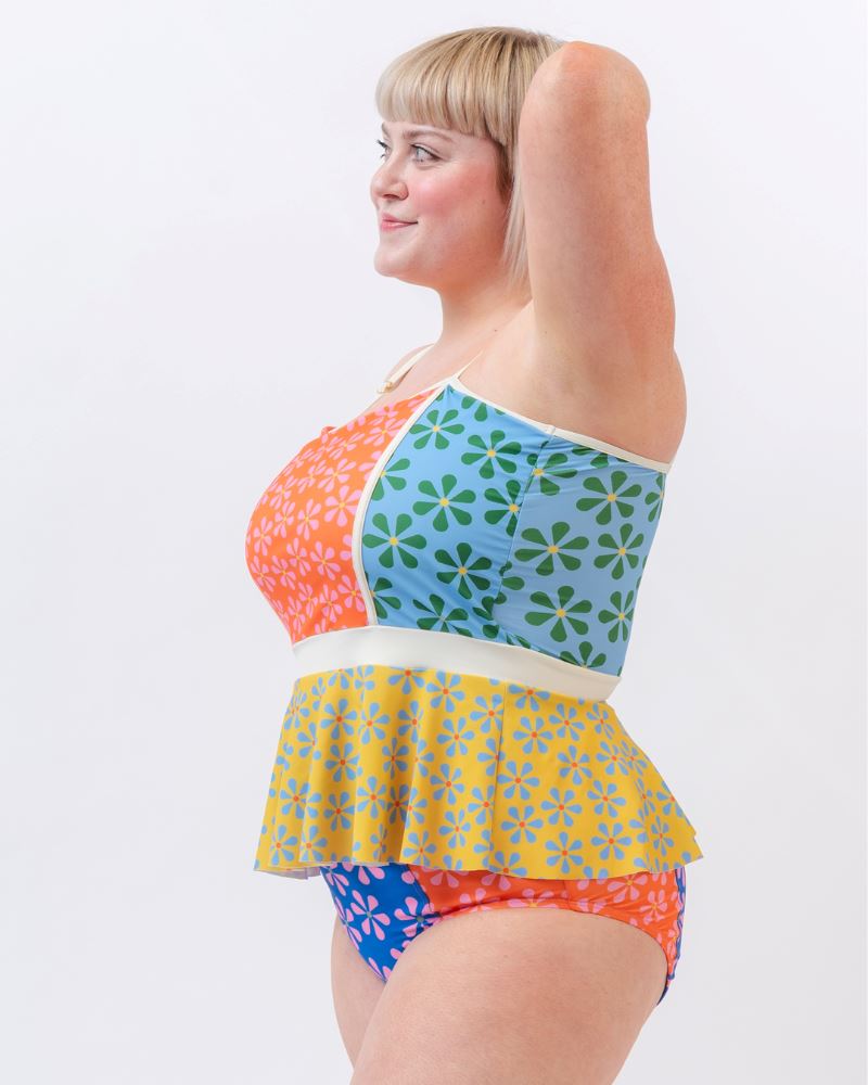 Photo of a woman wearing a multi-colored floral peplum swim top and a multi-colored floral swim bottom- side angle