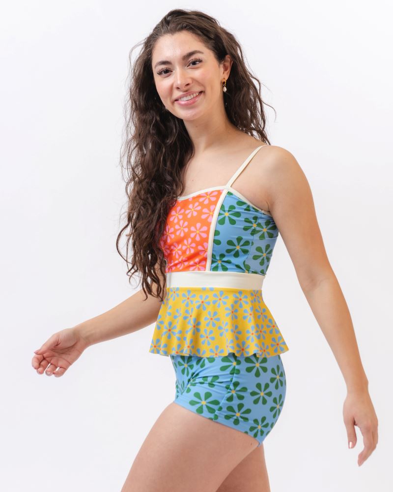 Photo of a woman wearing a multi-colored floral peplum swim top and a blue and green floral swim short bottom- side angle