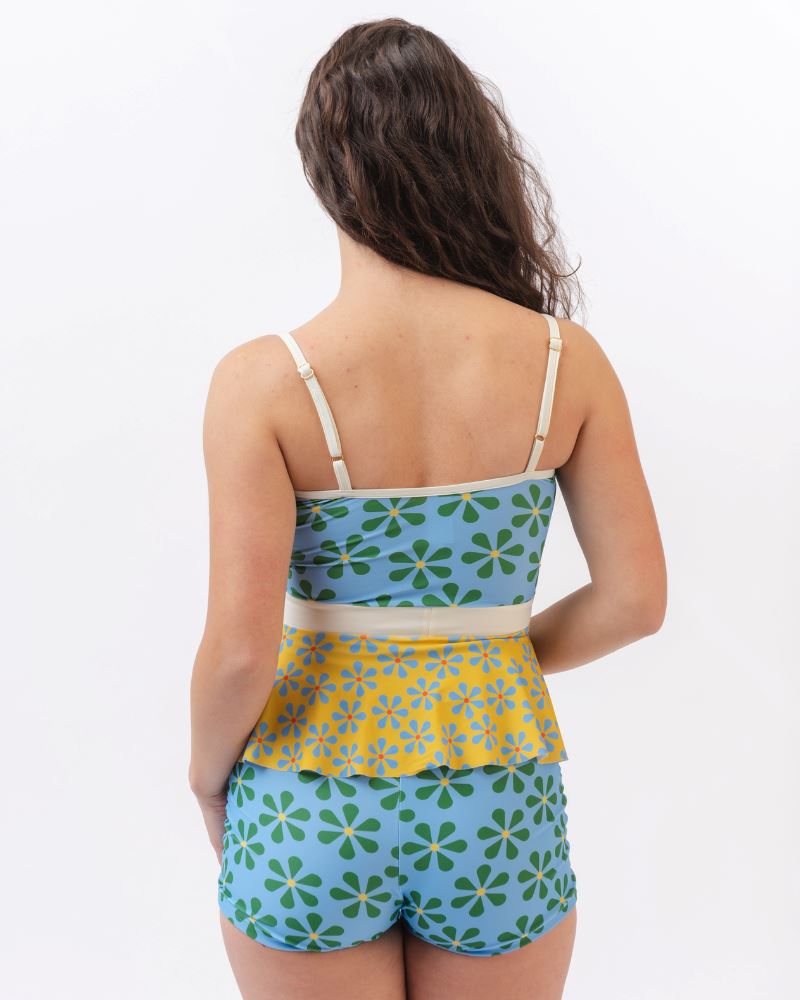Photo of a woman wearing a blue and green floral swim short bottom and a multi colored floral peplum swim top- back angle