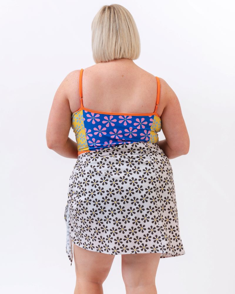 Photo of a woman wearing a black and white floral sarong and a multi colored one-piece swimsuit-back angle