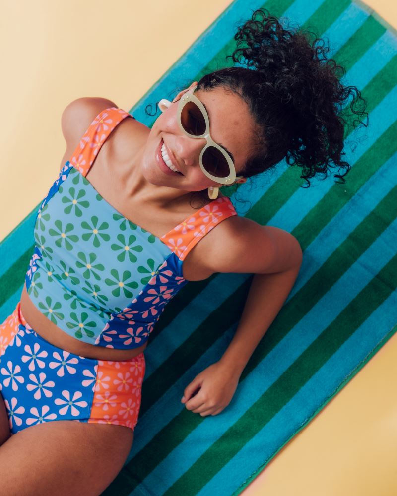 Photo of a woman laying on a beach towel wearing a multi-colored floral square neck swim crop top and a multi-colored floral swim bottom