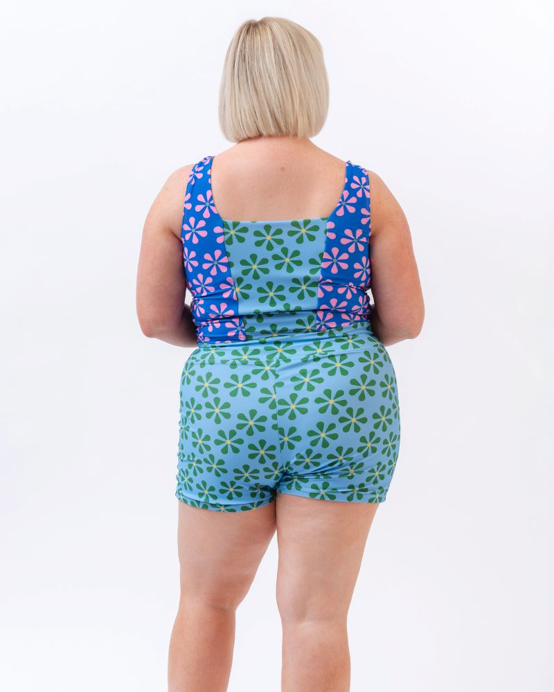 Photo of a woman wearing a blue and green floral swim short bottom and a multi colored floral swim crop top- back angle