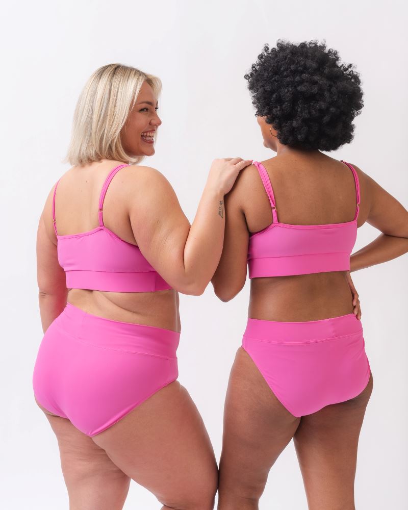 Photo of two women wearing dark pink swim bralettes and dark pink swim bottoms -back angle