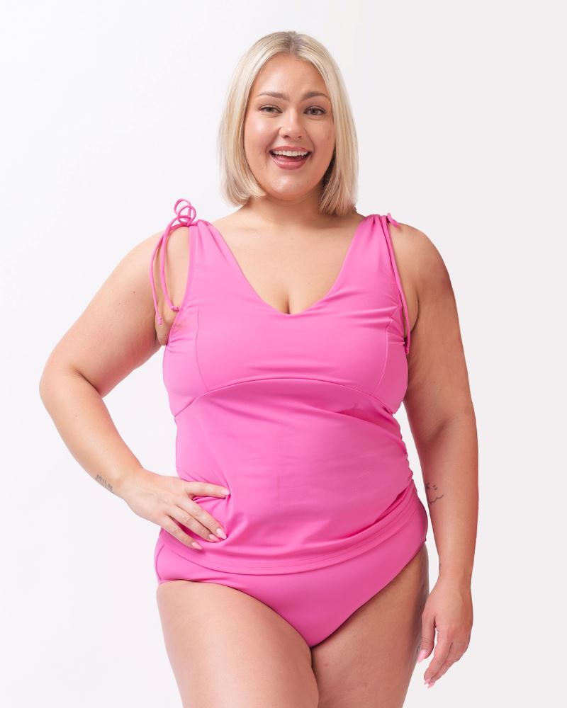 Photo of woman with her hand on her hip wearing a pink swim tankini with pink low waist swim bottoms