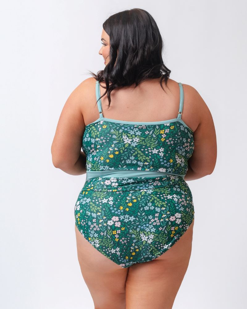 Photo of a woman wearing a dark green floral classic one-piece swimsuit- back angle