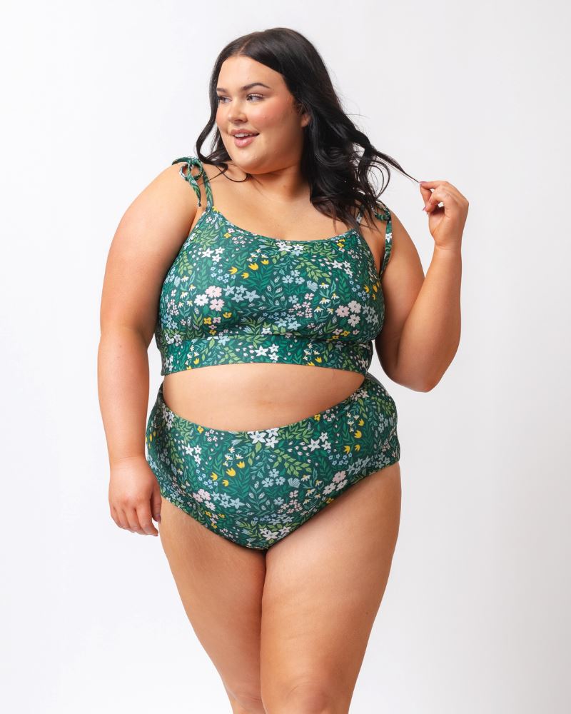 Photo of a woman wearing a dark green floral/ light green reversible swim bottom - floral side and a dark green floral shoulder-tie swim crop top