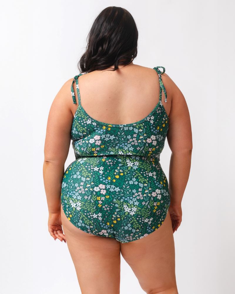Photo of a woman wearing a dark green floral/ light green reversible swim bottom - floral side and a dark green floral shoulder-tie swim crop top- back angle