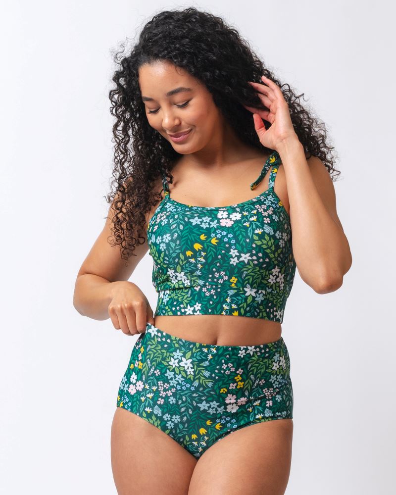 Photo of a woman wearing a dark green floral shoulder-tie swim crop top and a dark green flora/ light green reversible swim bottom- floral side