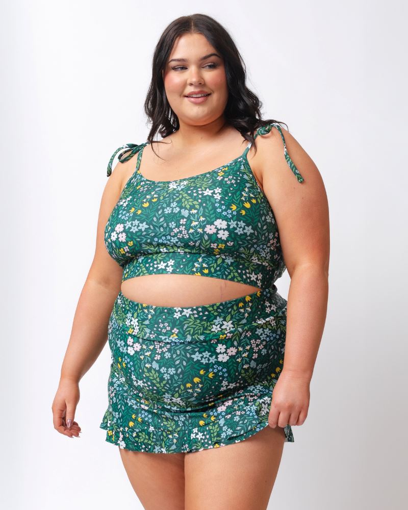 Photo of a woman wearing a dark green floral shoulder-tie swim crop top and a dark green floral swim skirt