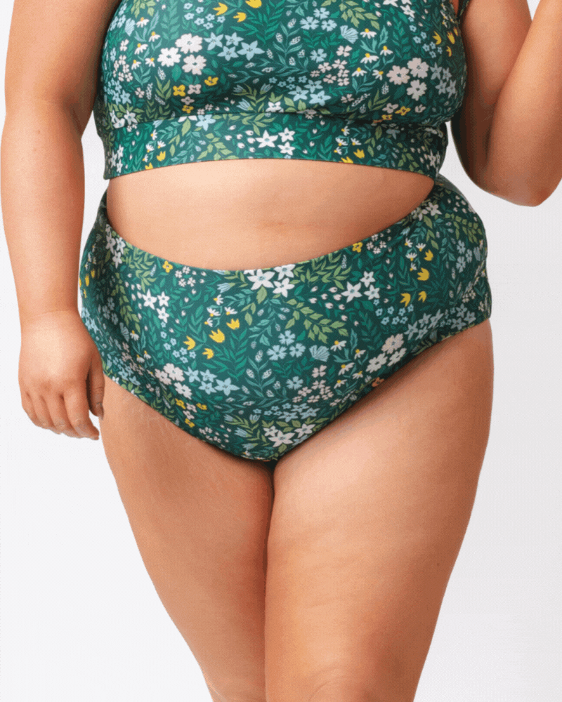 Close up GIF of a woman wearing a dark green floral/ light green reversible swim bottom