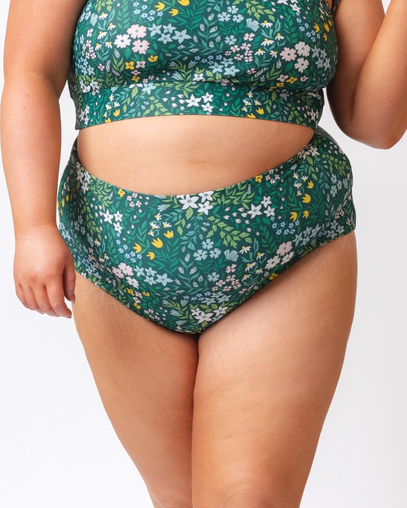 Close up photo of a woman wearing a dark green floral/ light green reversible swim bottom - floral side
