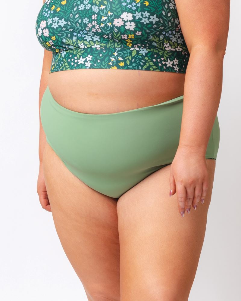 Close up photo of a woman wearing a dark green floral/ light green reversible swim bottom - light green side