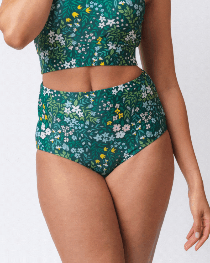 Close up GIF of a woman wearing a dark green floral/ light green reversible swim bottom