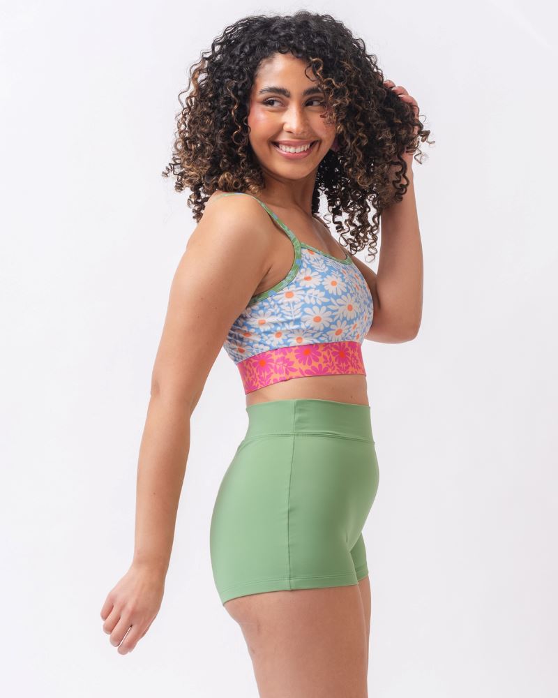 Photo of a woman from the side wearing a blue and pink floral cropped swim top with light green swim shorts