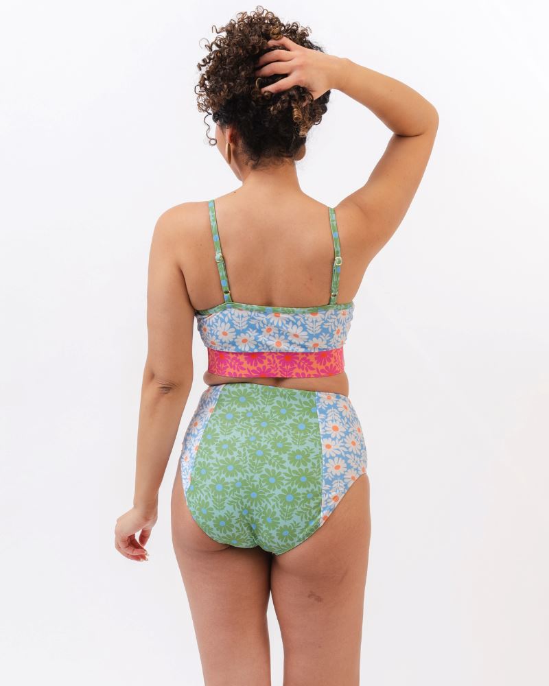 Photo of a woman with her back facing us wearing a blue and pink floral cropped swim top with blue and green floral high waist swim bottoms