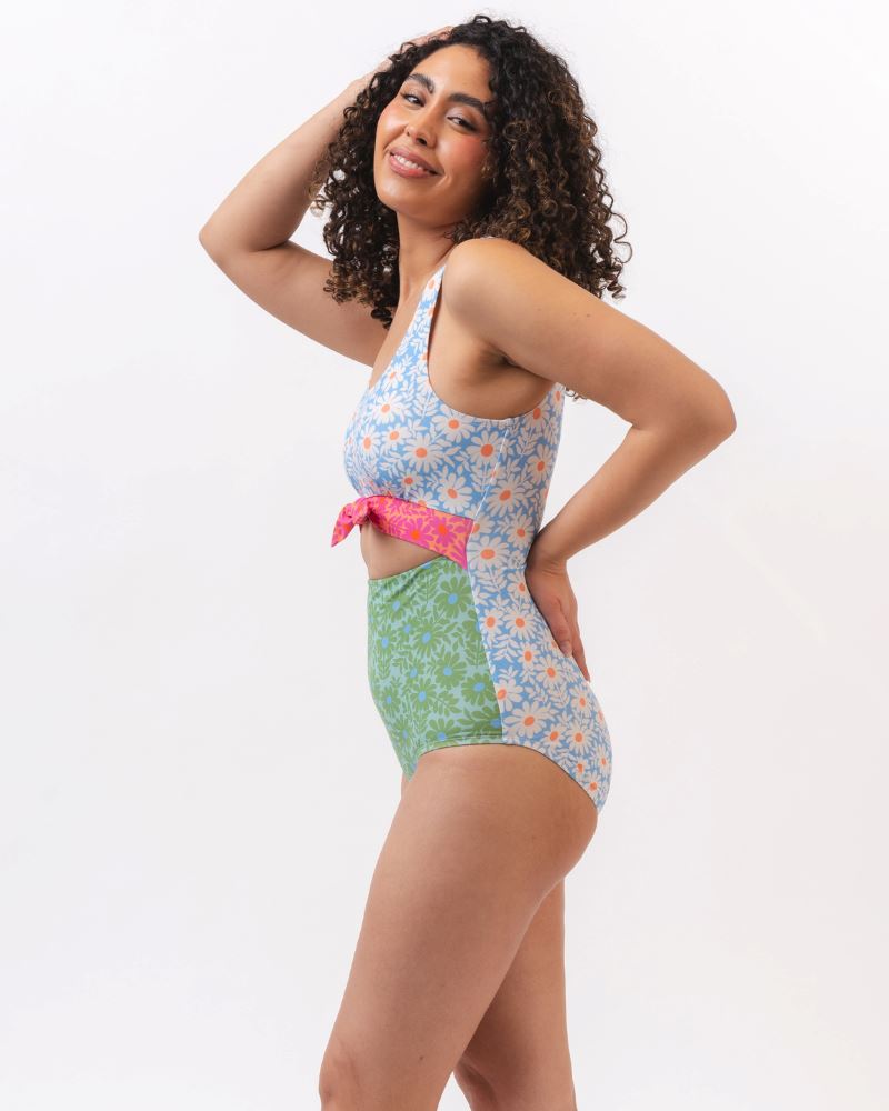 Photo of a woman from the side wearing a blue and green floral knotted one piece swim suit