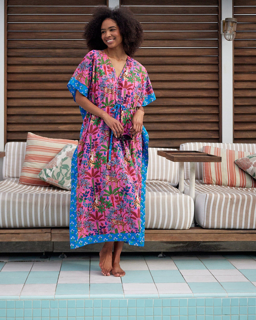 Photo of a woman posing outside wearing a bold pink and blue print featuring tigers and leopards caftan swim suit cover-up