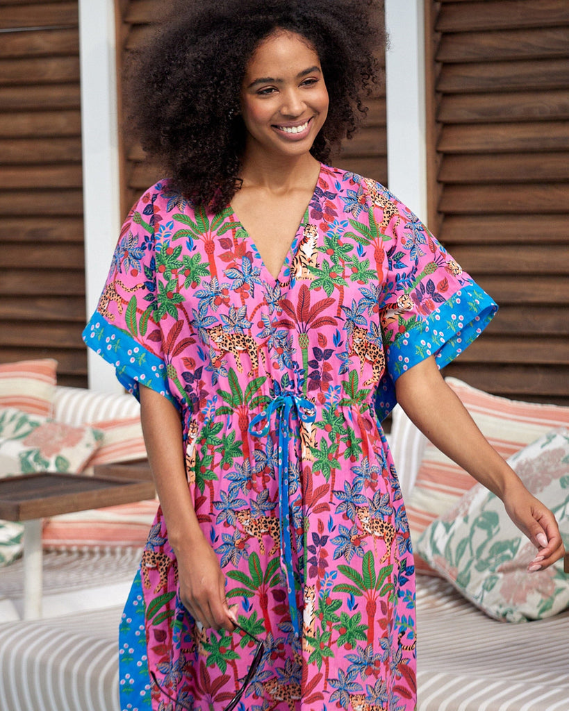 Photo of a woman posing outside wearing a bold pink and blue print featuring tigers and leopards caftan swim suit cover-up
