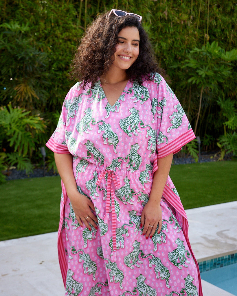 Close up photo of a woman standing by the pool wearing a bold pink and green tiger print long cover up