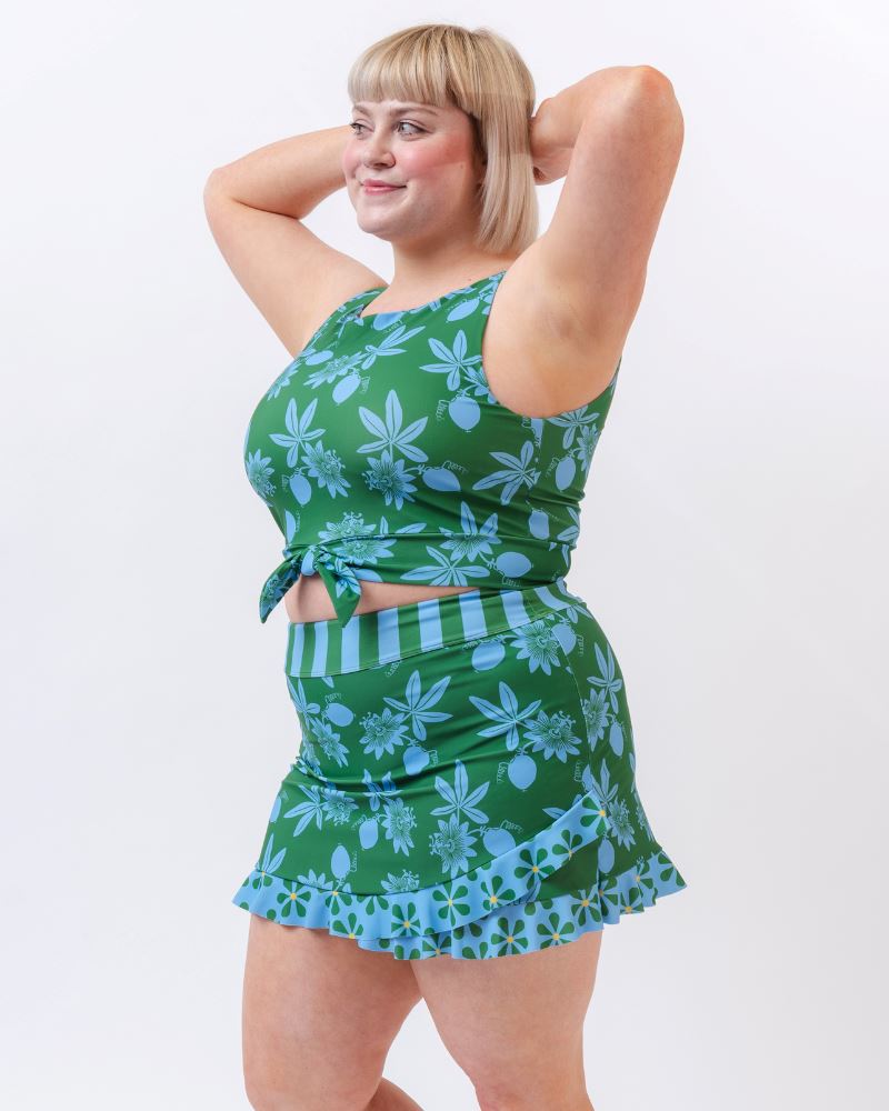 Photo of a woman wearing a green and blue floral swim crop top and a green and blue floral swim skirt bottom- side angle