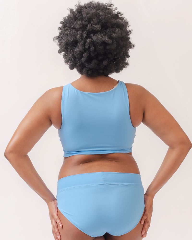 Photo of a woman wearing a light periwinkle blue knotted swim crop top and a light periwinkle blue classic swim bottom- back angle