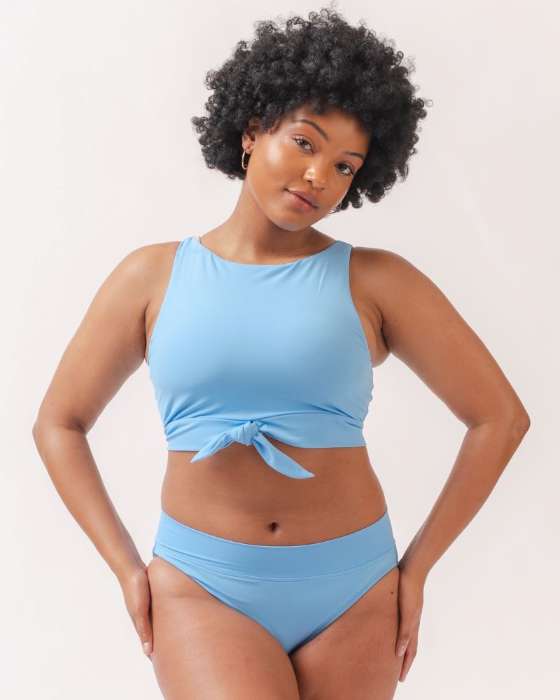 Photo of a woman wearing a light periwinkle blue knotted swim crop top and a light periwinkle blue classic swim bottom