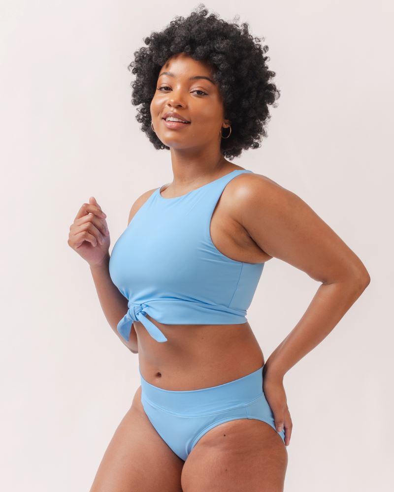 Photo of a woman wearing a light periwinkle blue knotted swim crop top and a light periwinkle blue classic swim bottom- side angle