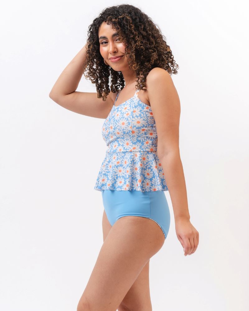 Photo of a woman from the side wearing a blue floral tankini swim top with light blue high waist swim bottoms