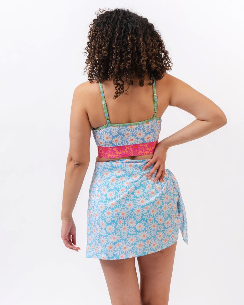 Photo of a woman with her back facing us  wearing a blue and pink floral cropped swim top with a blue floral sarong tied at her waist