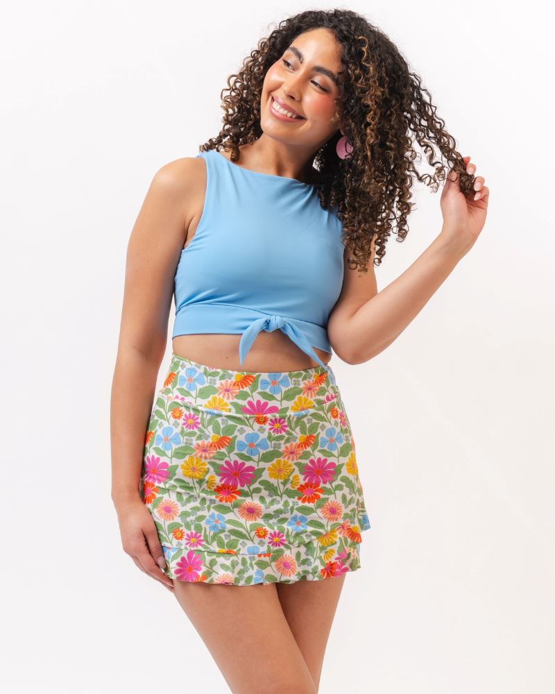 Photo of a woman wearing a light blue cropped swim top with a multi colored floral swim skirt